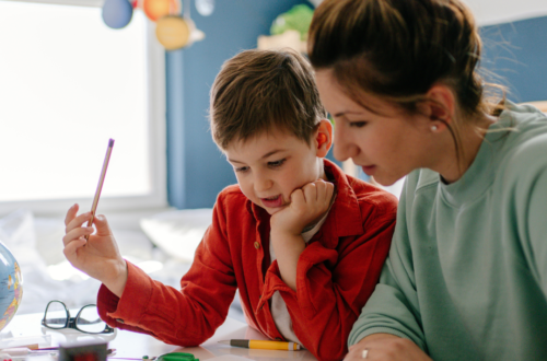 A mother calmly helping her young son with schoolwork at a desk, illustrating a stress-free approach to parenting and daily educational routines.