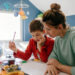 A mother calmly helping her young son with schoolwork at a desk, illustrating a stress-free approach to parenting and daily educational routines.